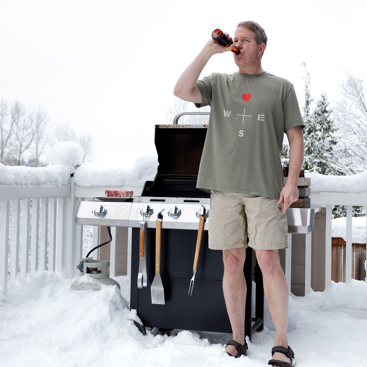 Man wearing a heart compass t-shirt from the outdoor brand Northling drinking beer and grilling in the snow.